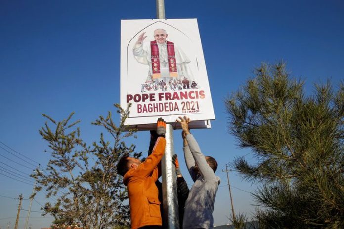 Voluntarios colocan un cartel sobre la visita del Papa en Bagdad